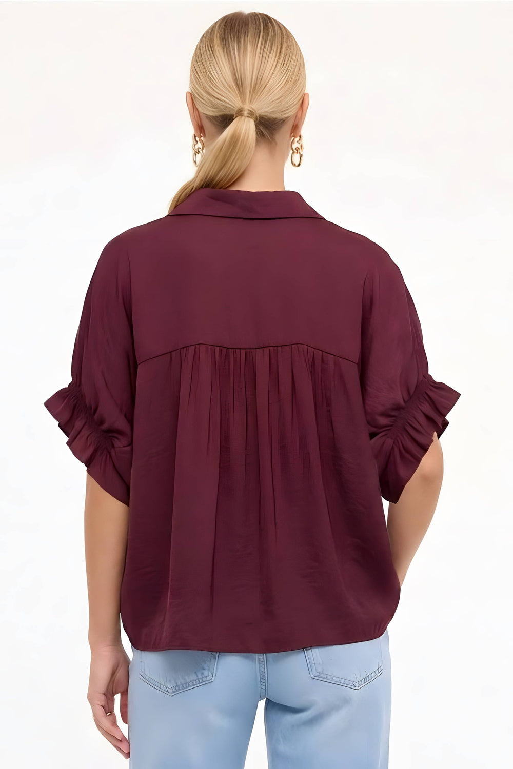 A woman viewed from the back wearing a burgundy short-sleeve blouse with ruffled cuffs and a gathered seam across the upper back, paired with light blue jeans against a plain white background.
