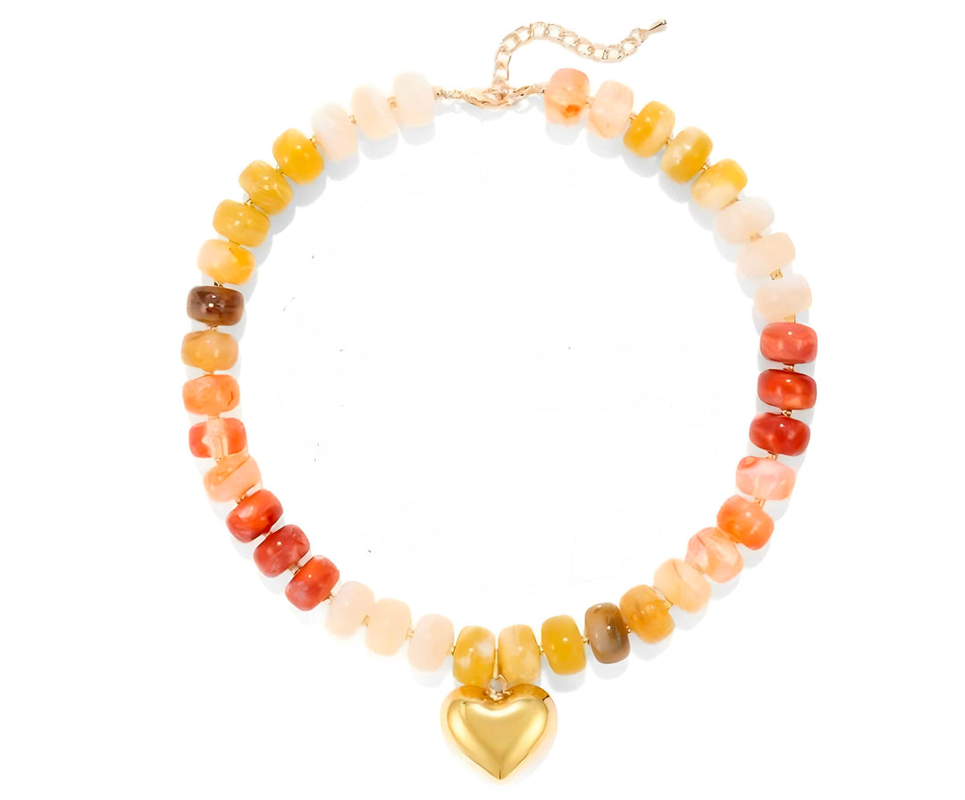 A beaded necklace featuring a gradient of stone beads transitioning from pale cream to orange, red, and yellow, finished with a polished gold heart pendant and chain.