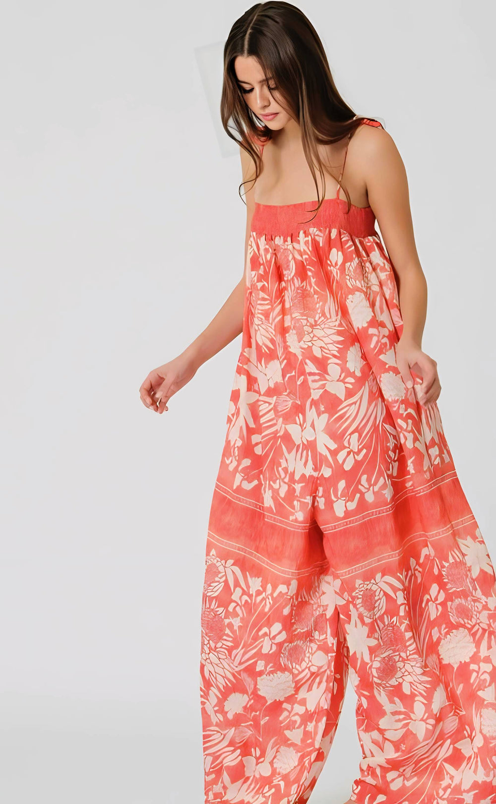 Woman wearing a coral floral jumpsuit on a white background