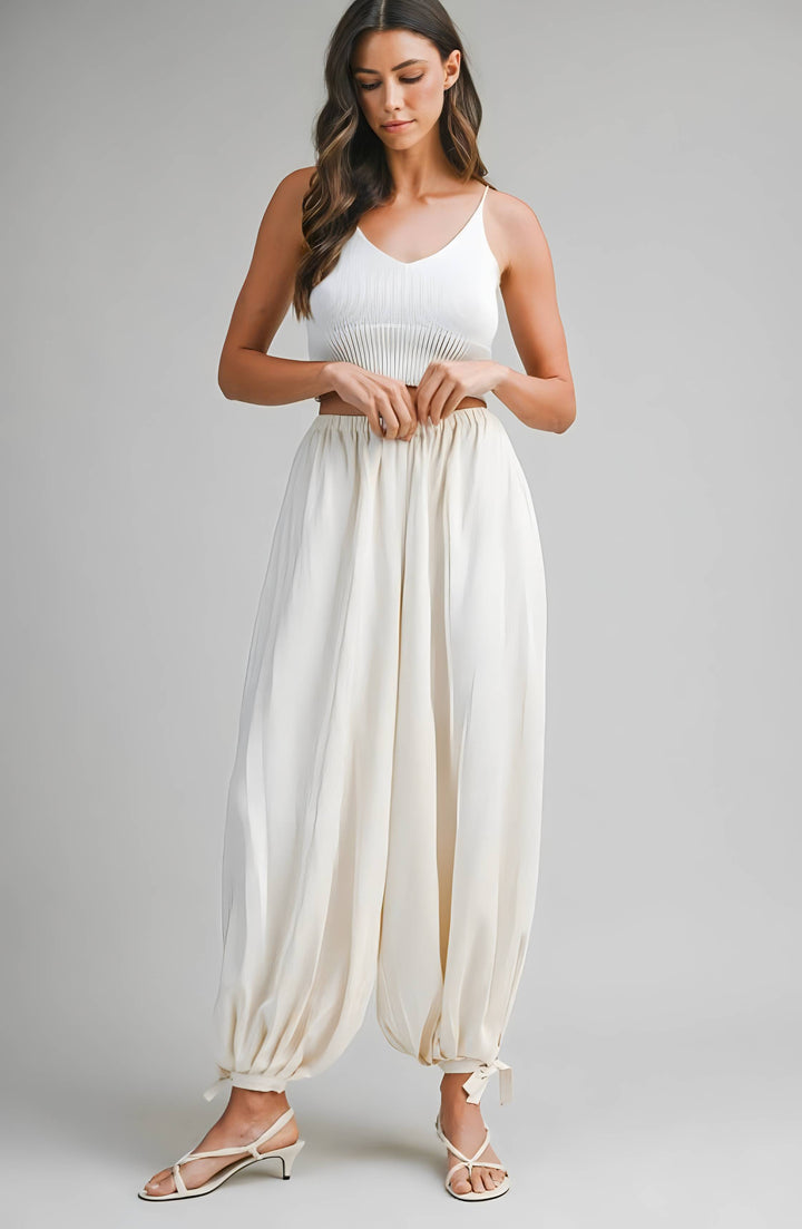 Woman wearing a cream sleeveless top and wide-leg pants on a gray background