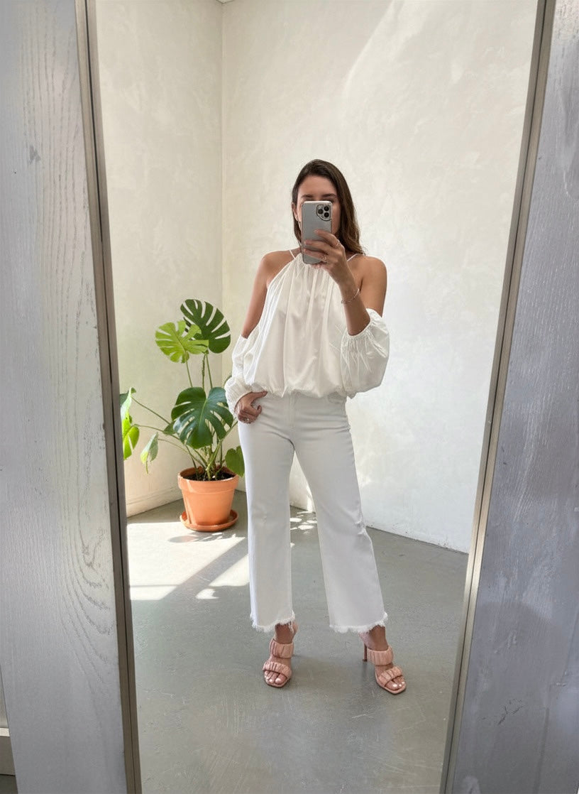Woman taking a mirror selfie wearing a white top and pants in a room with a plant.