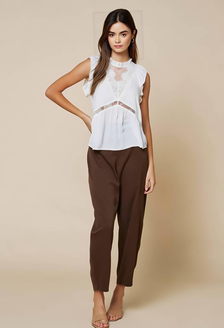 Woman wearing a white blouse and brown pants on a beige background