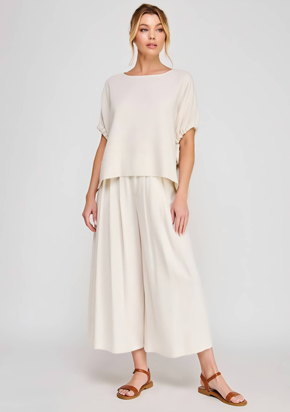 Woman wearing a white outfit with wide-leg pants on a plain background