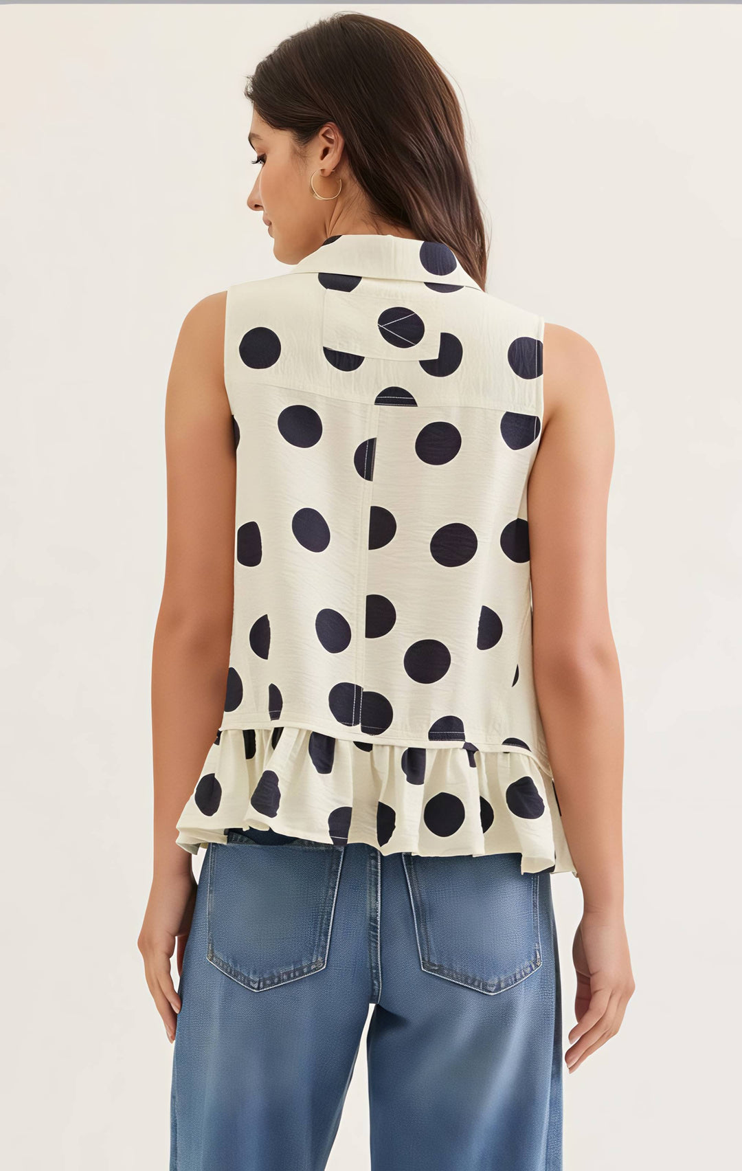 Woman wearing a sleeveless polka dot top and blue jeans on a plain background