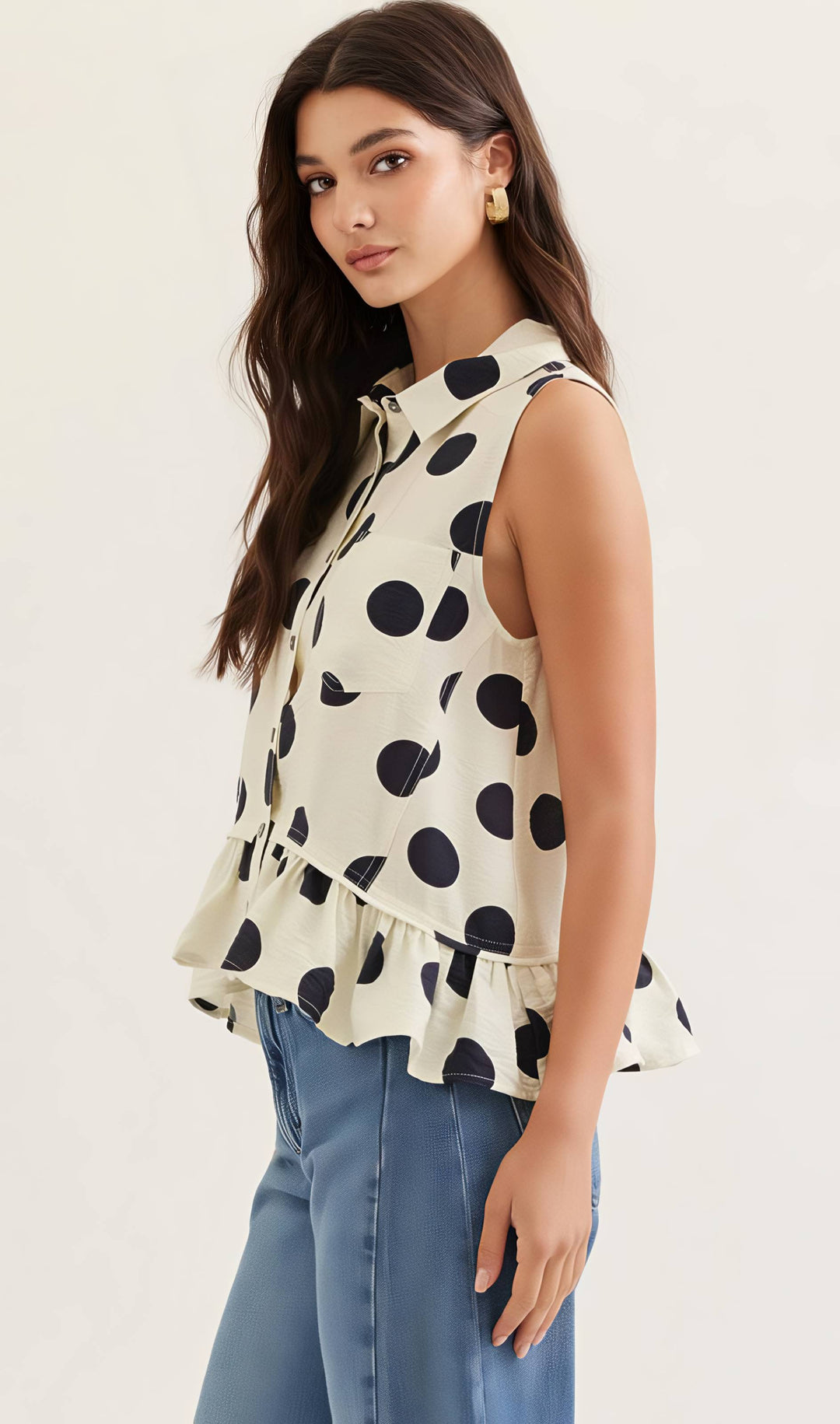 Woman wearing a sleeveless polka dot blouse with blue jeans on a white background