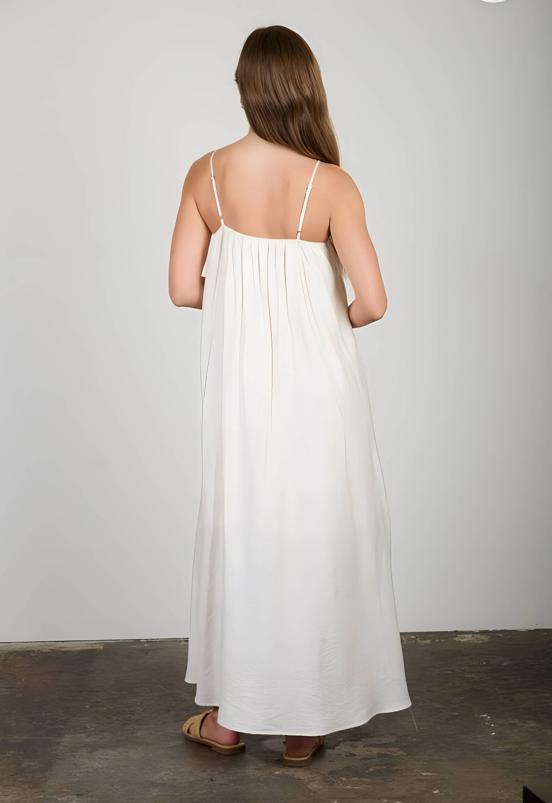 Woman wearing a white dress with thin straps against a plain background