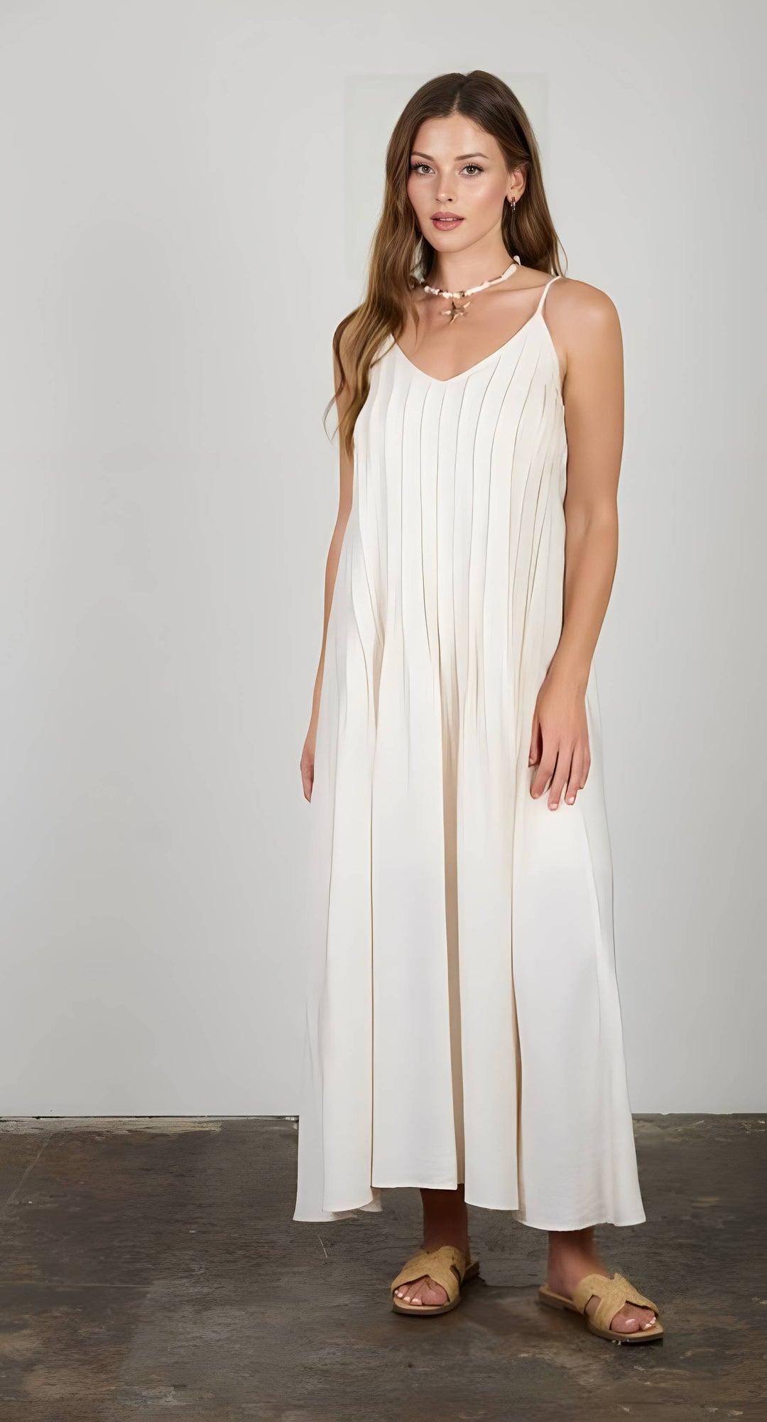 Woman wearing a white dress with thin straps against a plain background