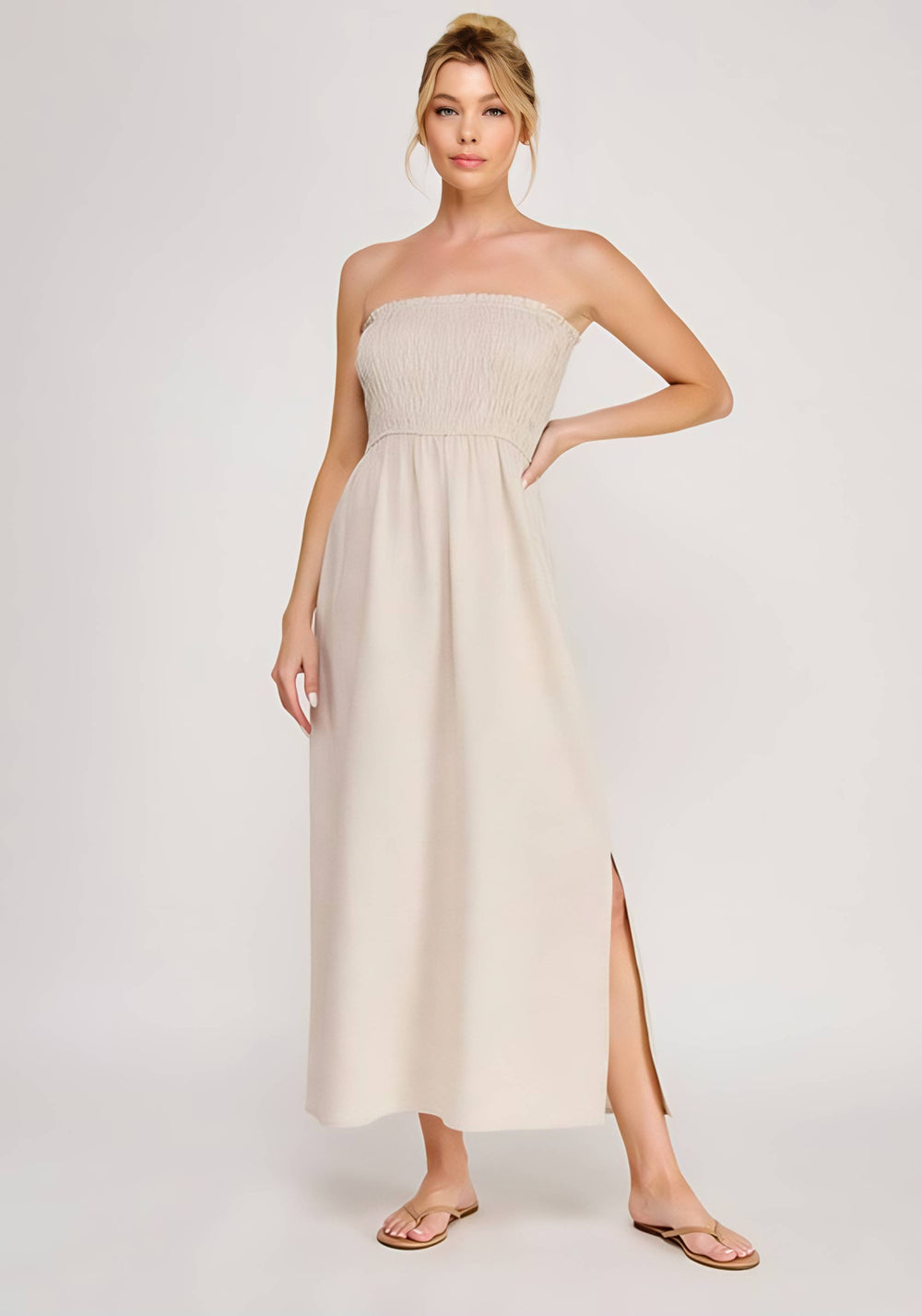 Woman wearing a strapless beige dress with a slit on a white background