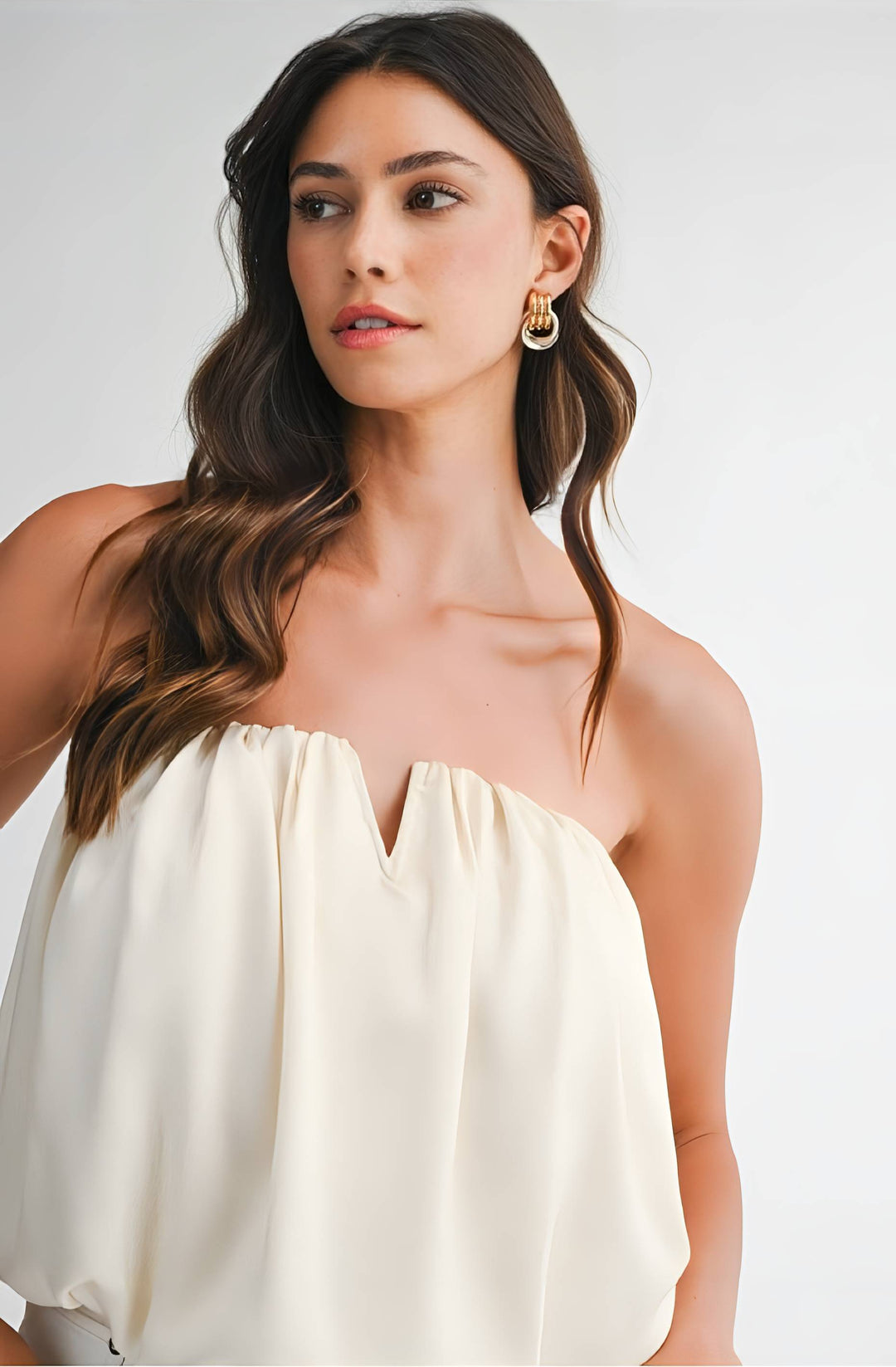 Woman wearing a strapless beige top against a plain background