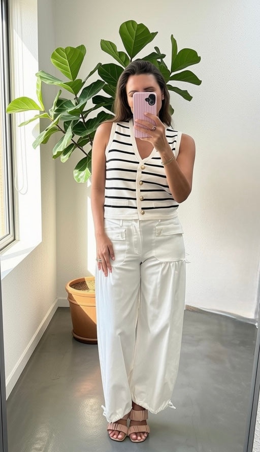 Woman wearing a cream and black stripe vest top with white flare jeans with a white background.