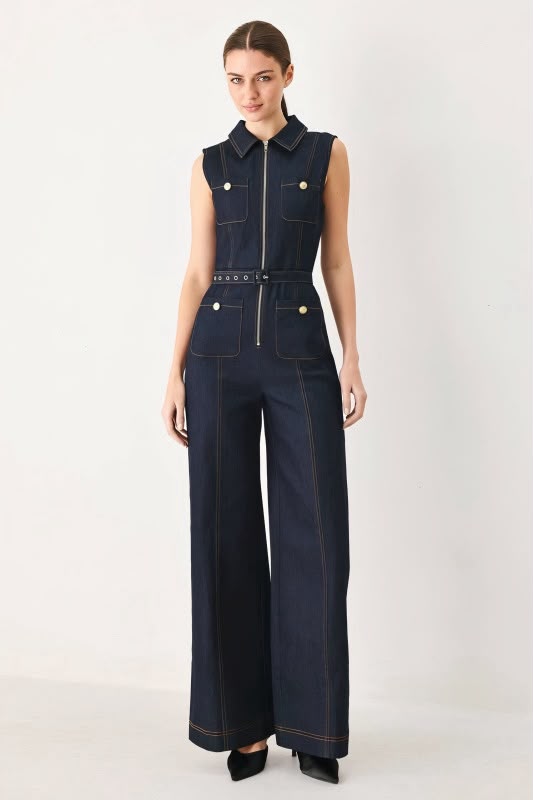 A woman viewed from the back wearing a sleeveless dark navy wide-leg jumpsuit with a matching waist tie, photographed against a light gray studio background.