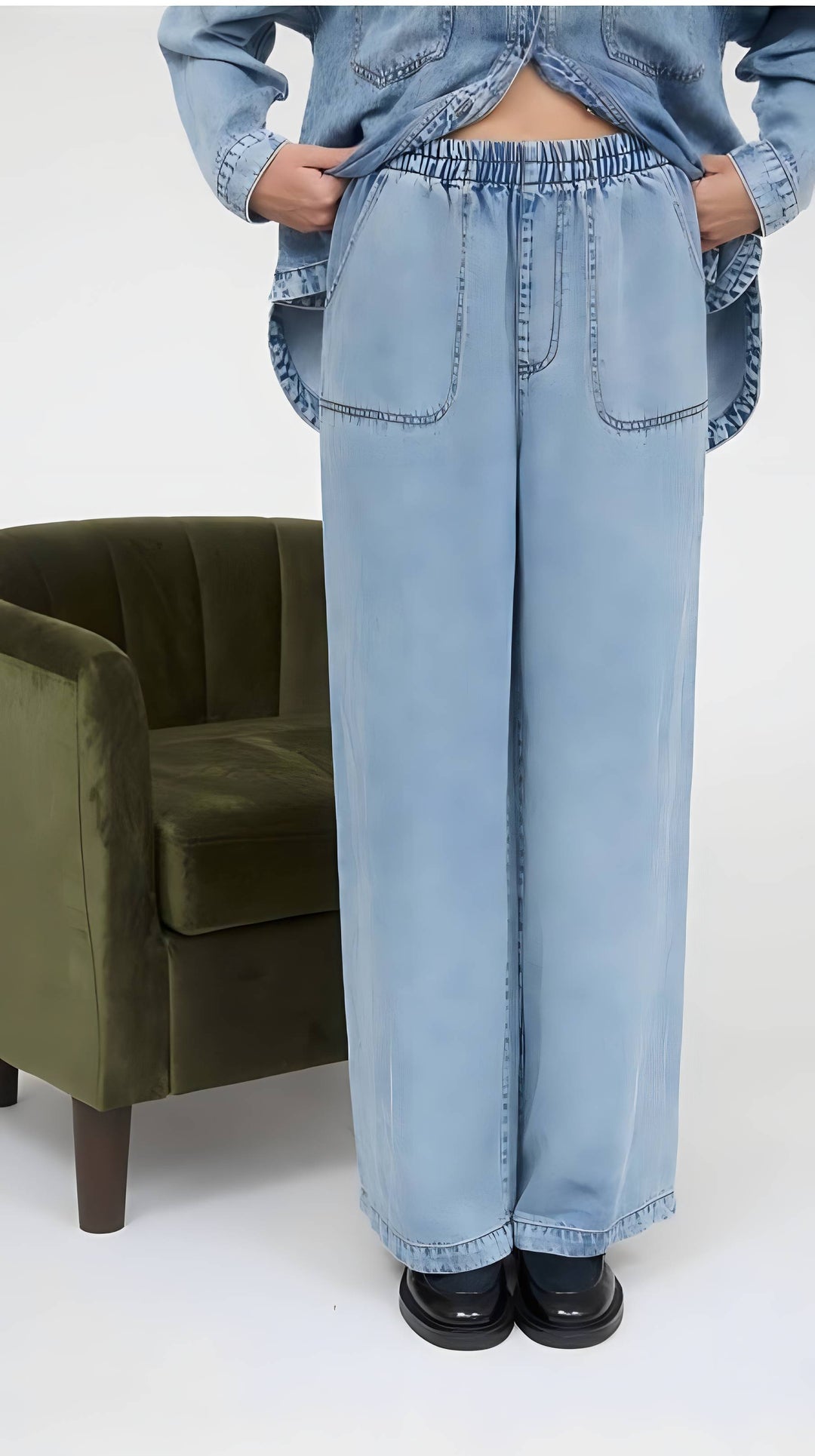 Person wearing light blue jeans and a denim jacket in a minimalistic setting with a green chair.