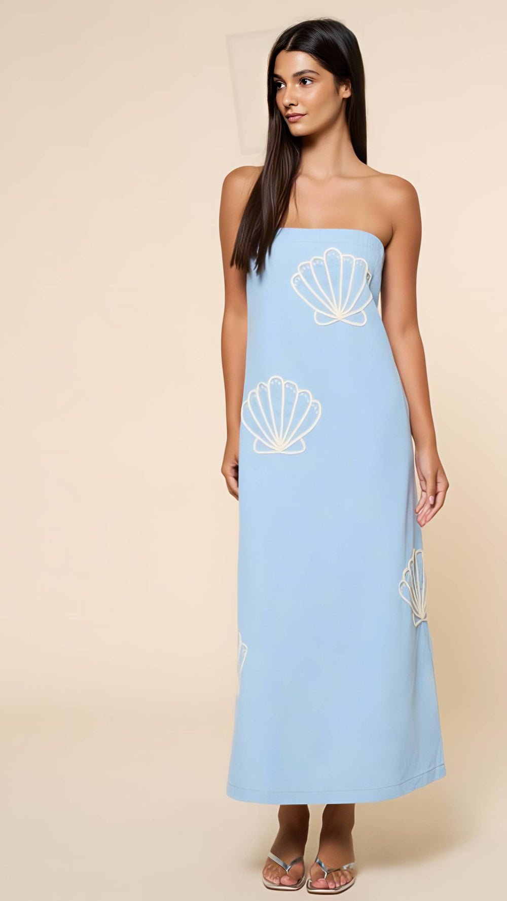 Woman wearing a light blue strapless dress with shell patterns on a beige background