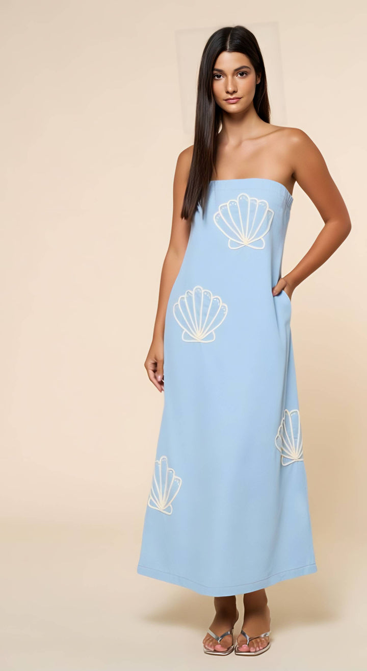 Woman wearing a light blue strapless dress with shell patterns on a beige background