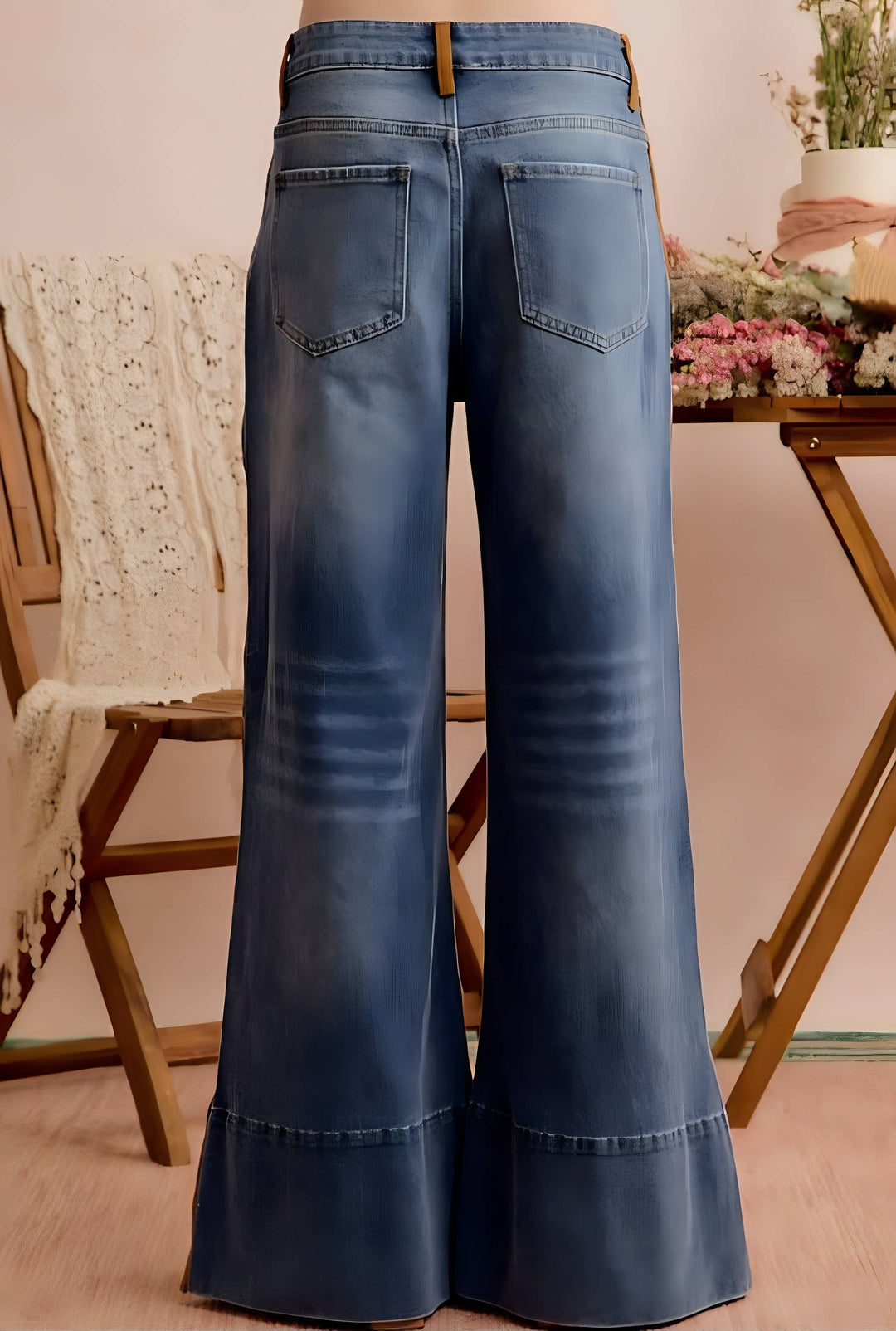 Blue wide-leg denim jeans shown from the back, featuring a faded wash and classic pocket design, displayed on a wooden stand in a styled indoor setting.