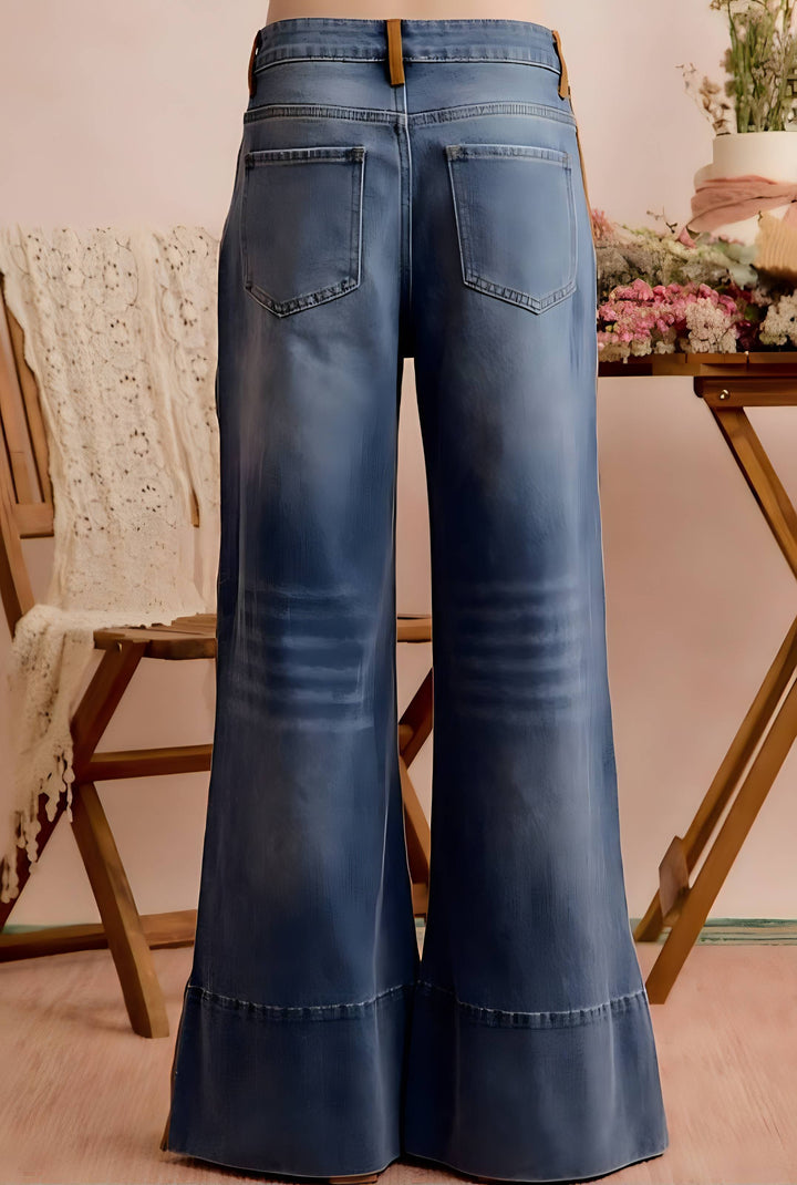 Blue wide-leg denim jeans shown from the back, featuring a faded wash and classic pocket design, displayed on a wooden stand in a styled indoor setting.