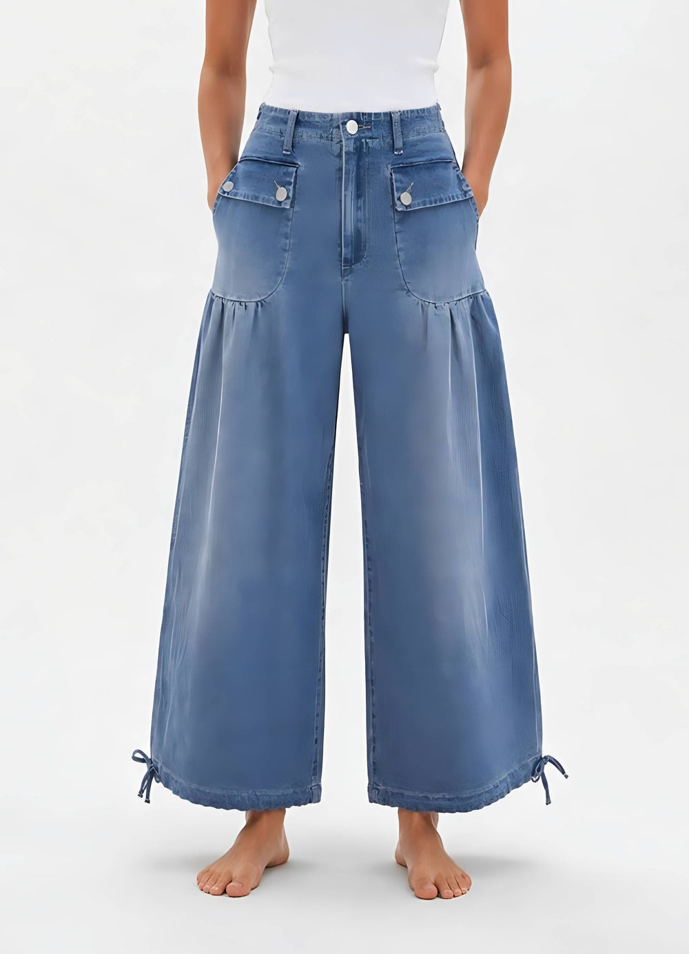 A model wearing high-waisted, wide-leg blue denim jeans with decorative front patch pockets and drawstring ankle cuffs, shown against a plain light gray studio background.