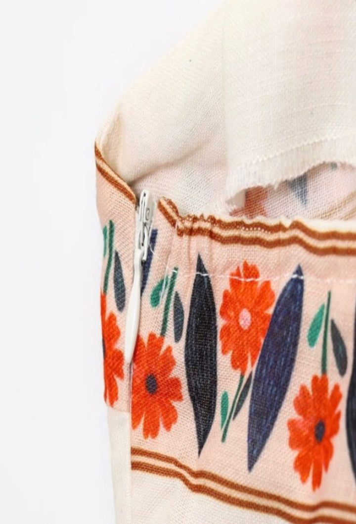 Close-up of a floral-patterned fabric with red flowers and green leaves on a beige background.