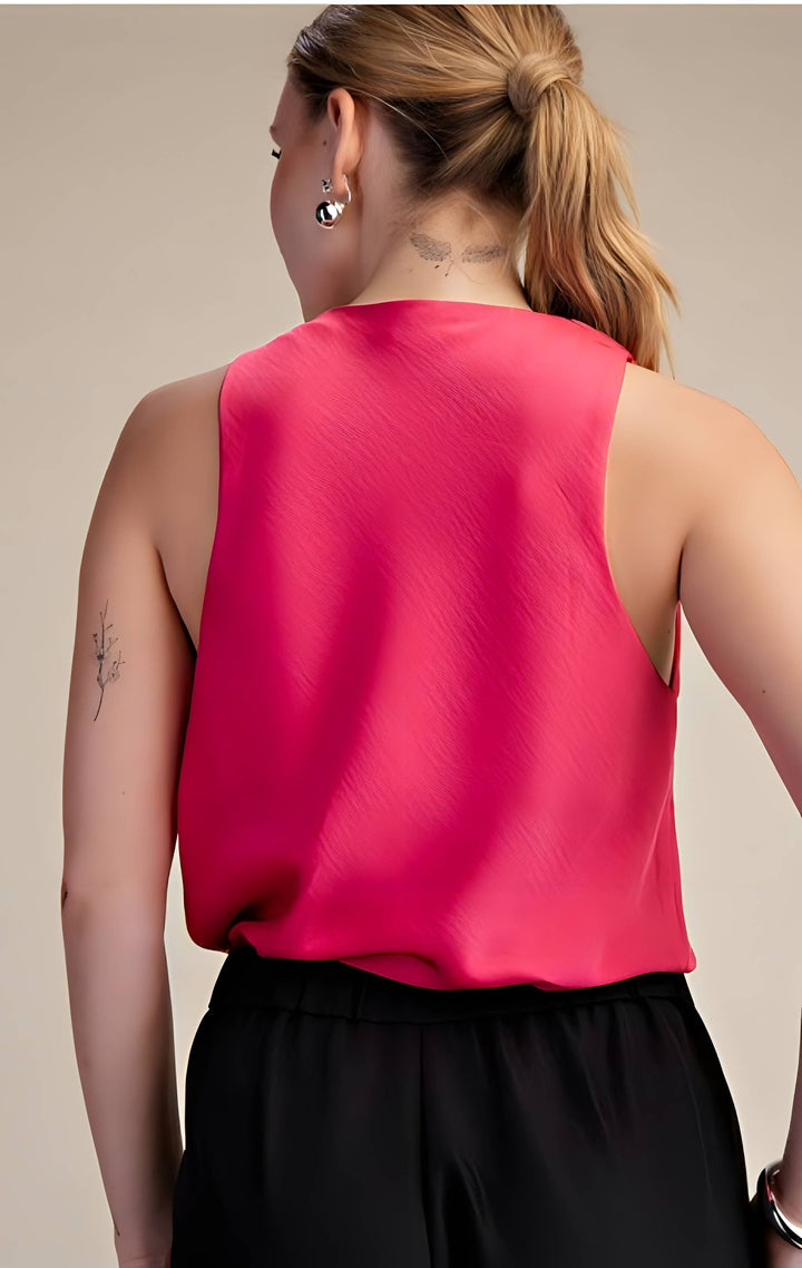 Person wearing a bright pink sleeveless top and black pants on a beige background