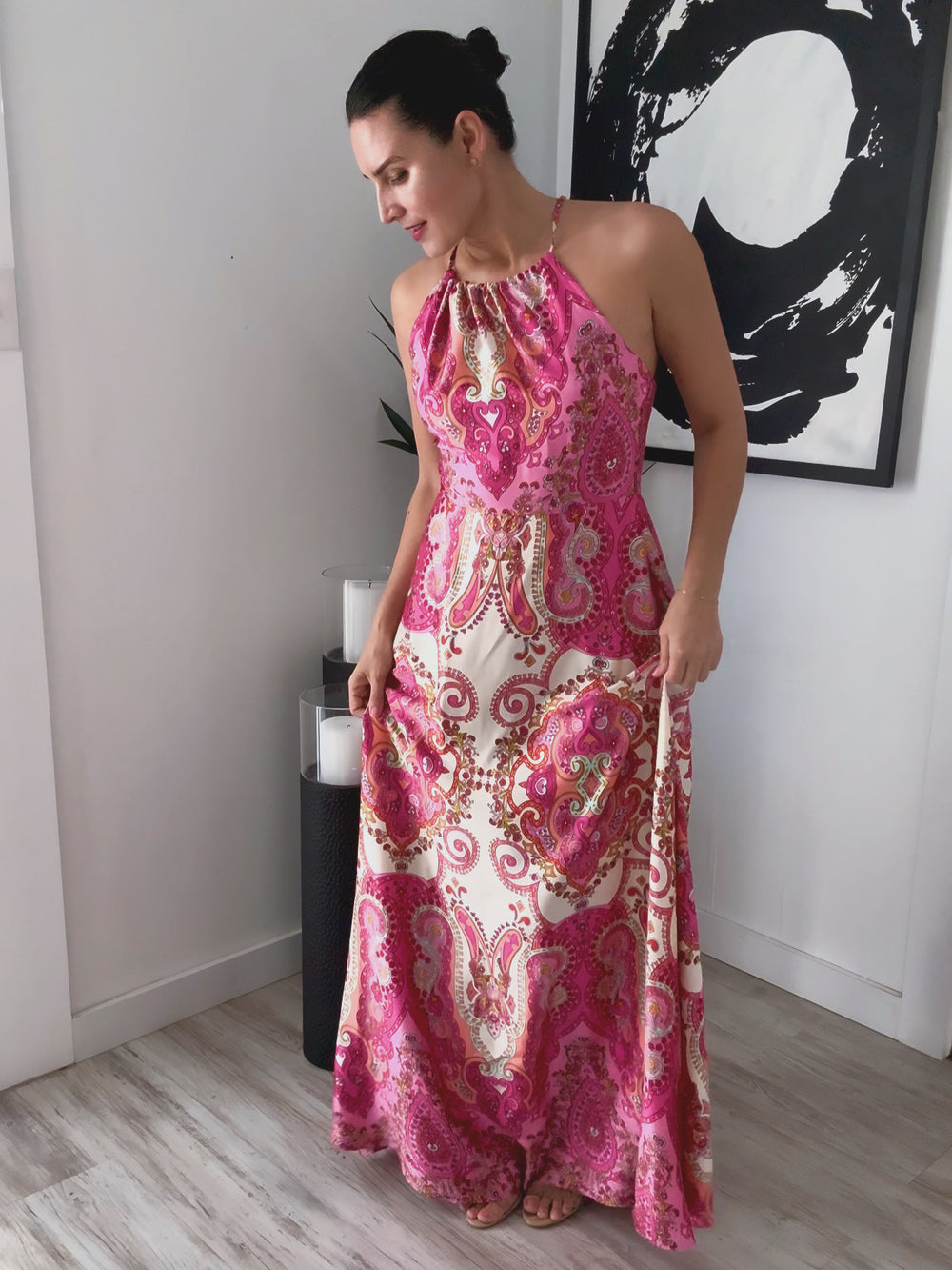 Woman wearing a pink and white patterned dress standing in a room with a black and white abstract painting on the wall.