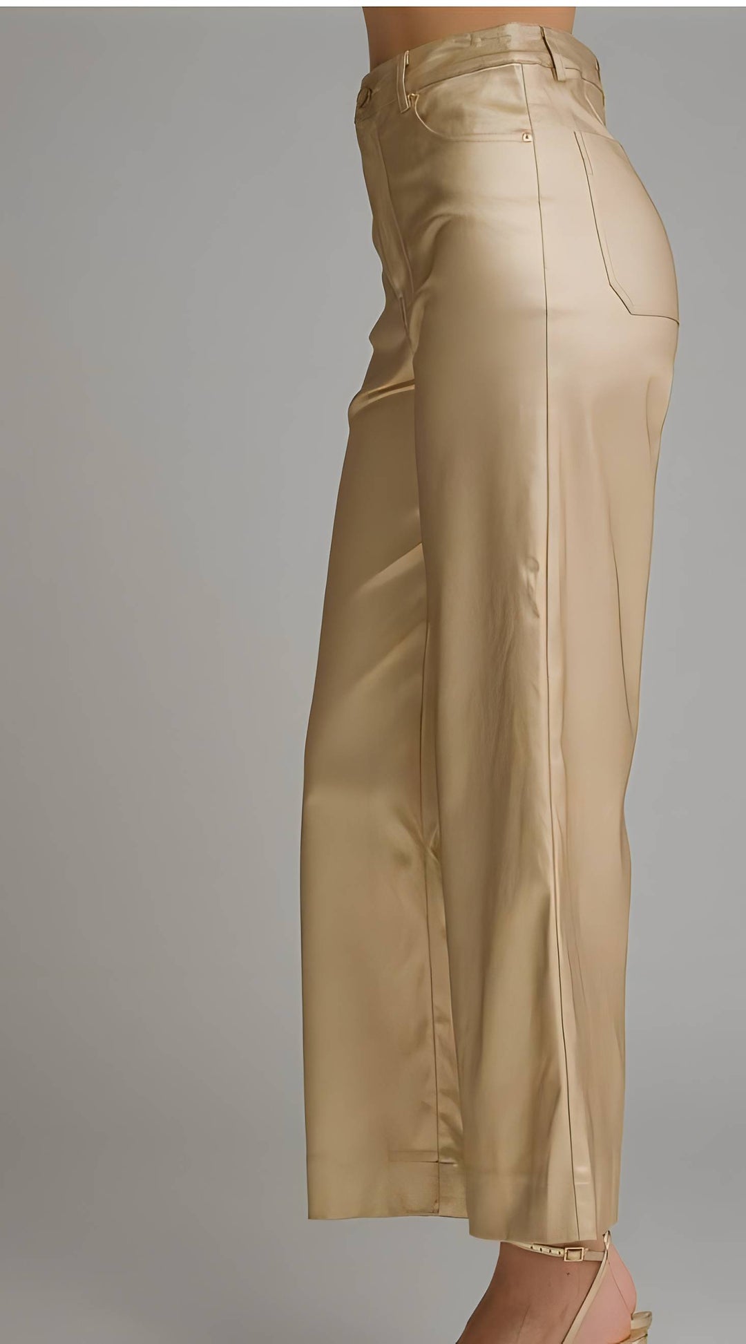 A side view of a model wearing high-waisted, wide-leg cropped pants in a shiny champagne-gold satin fabric, set against a plain gray studio background.