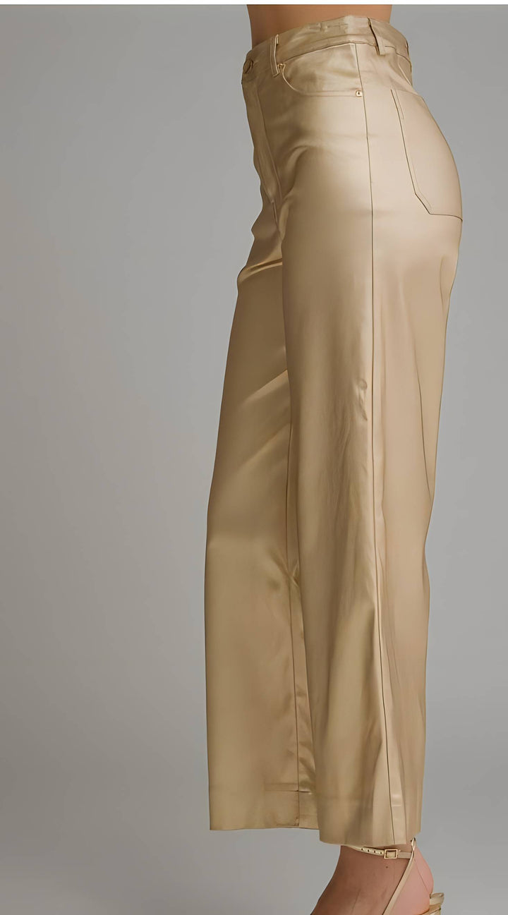 A side view of a model wearing high-waisted, wide-leg cropped pants in a shiny champagne-gold satin fabric, set against a plain gray studio background.