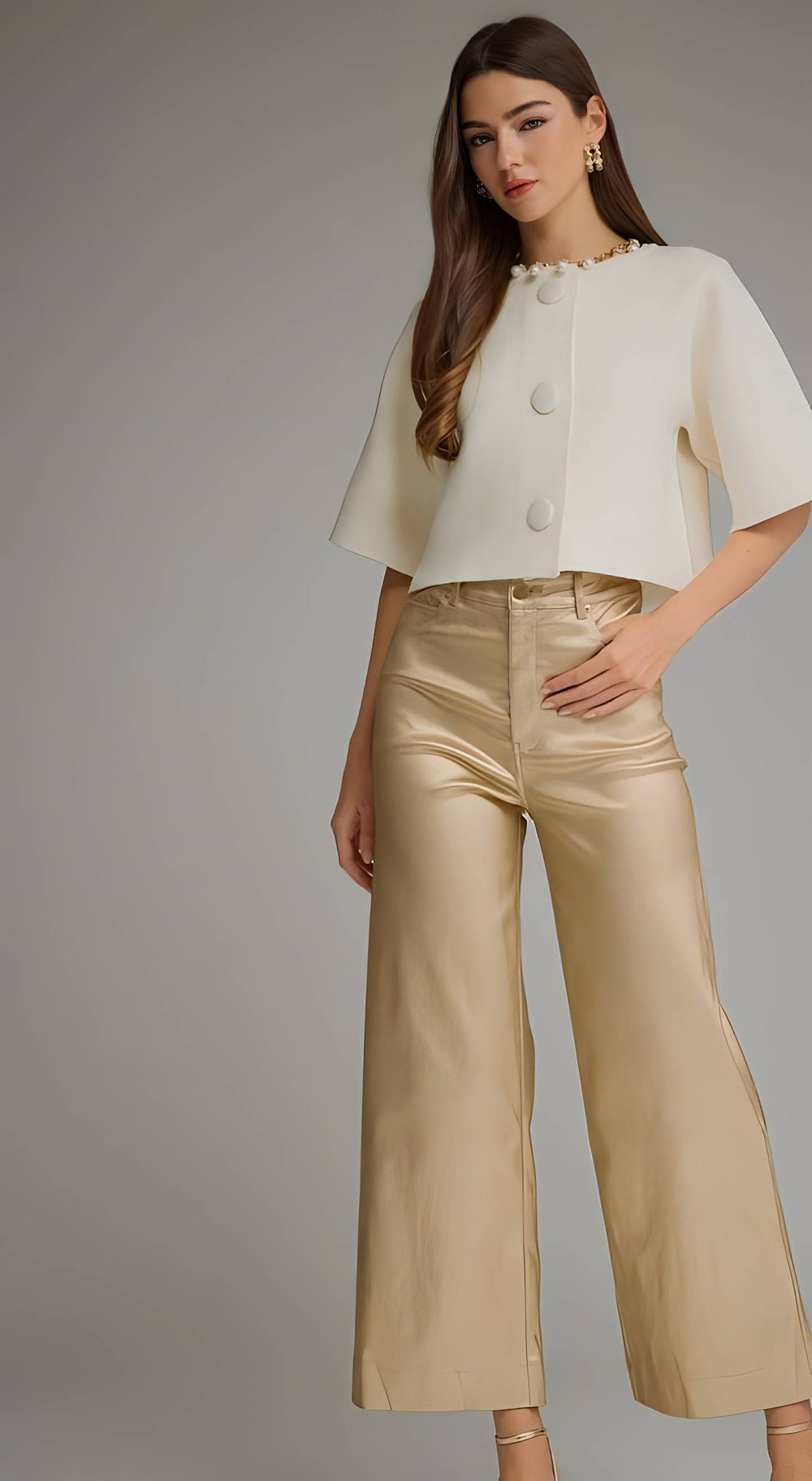 A woman modeling a cream short-sleeve cropped top with decorative buttons and high-waisted metallic champagne wide-leg pants against a neutral gray studio background.