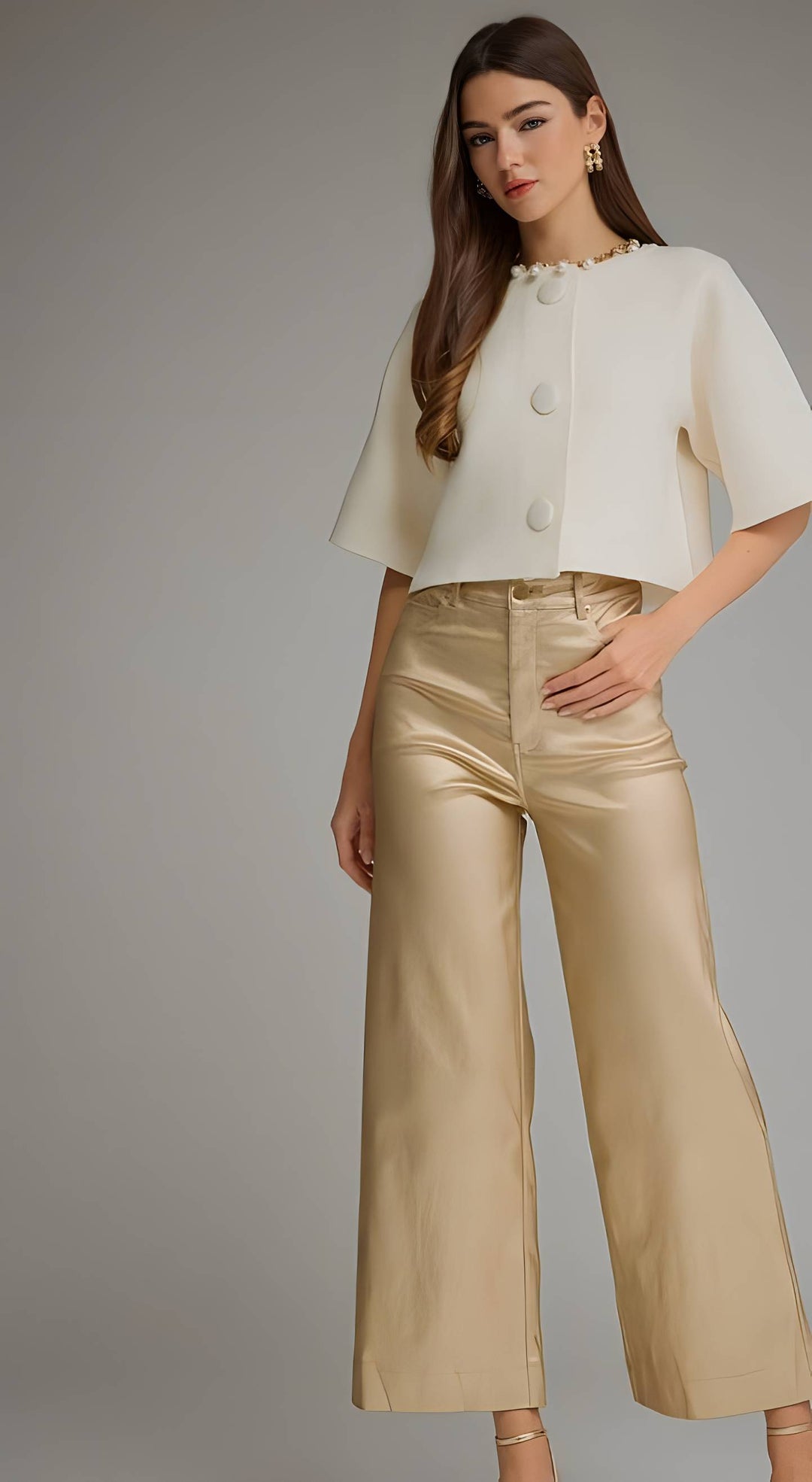 A woman modeling a cream short-sleeve cropped top with decorative buttons and high-waisted metallic champagne wide-leg pants against a neutral gray studio background.