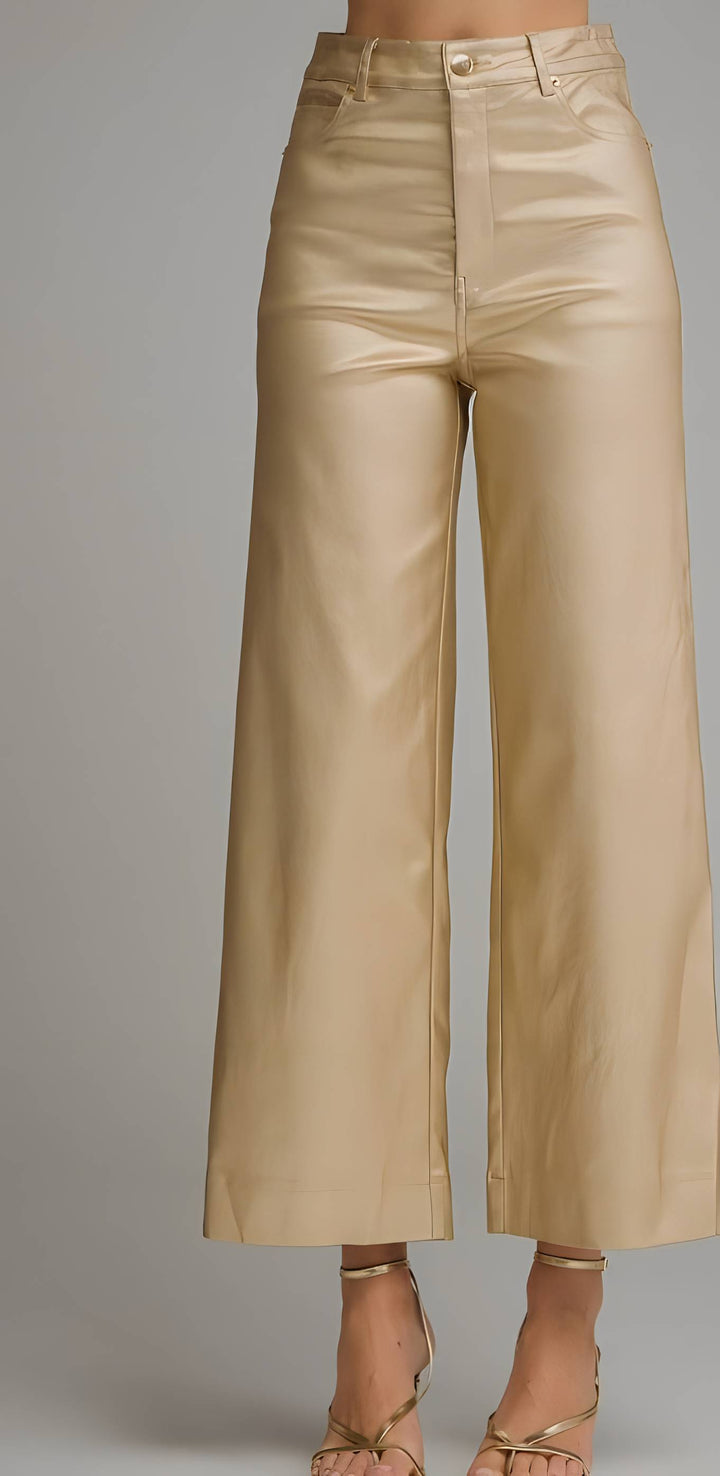 A model is wearing a pair of high-waisted, wide-leg cropped pants in a shiny champagne-gold fabric, paired with matching metallic gold strappy high-heeled sandals, set against a plain gray studio background.