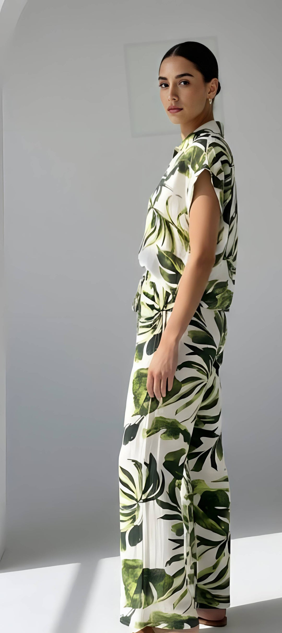 Woman wearing a green and white leaf-patterned jumpsuit against a plain background