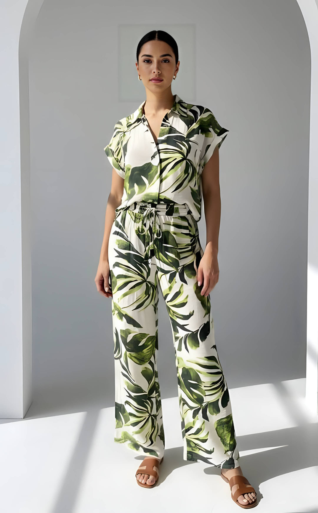 Woman wearing a tropical leaf patterned jumpsuit standing against a white background