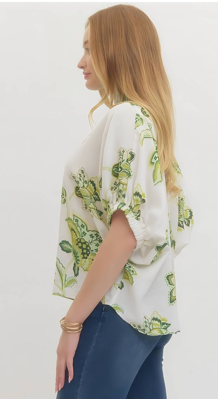Woman wearing a white blouse with green floral pattern on a plain background