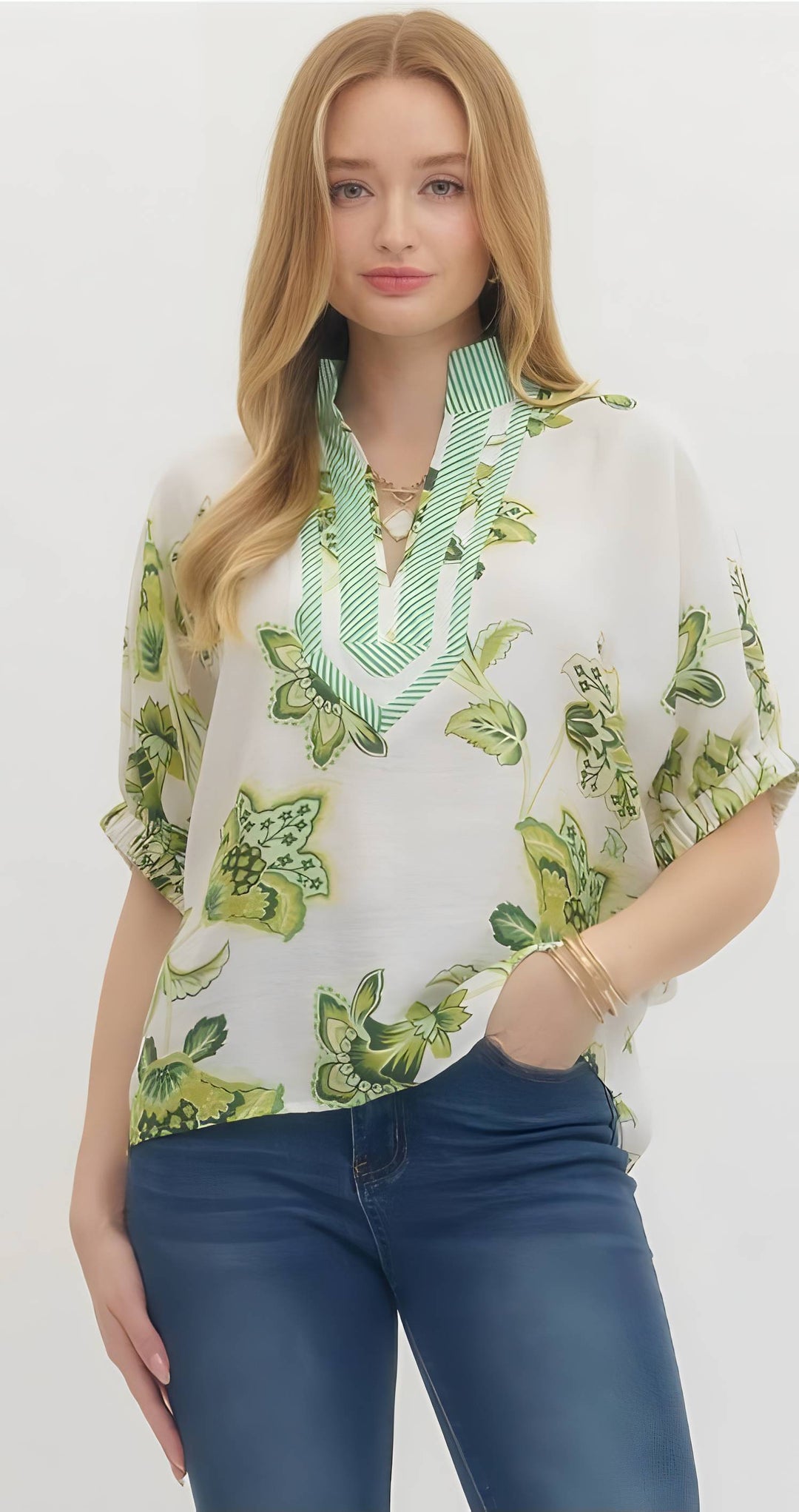 Woman wearing a white blouse with green leaf pattern and blue jeans on a white background