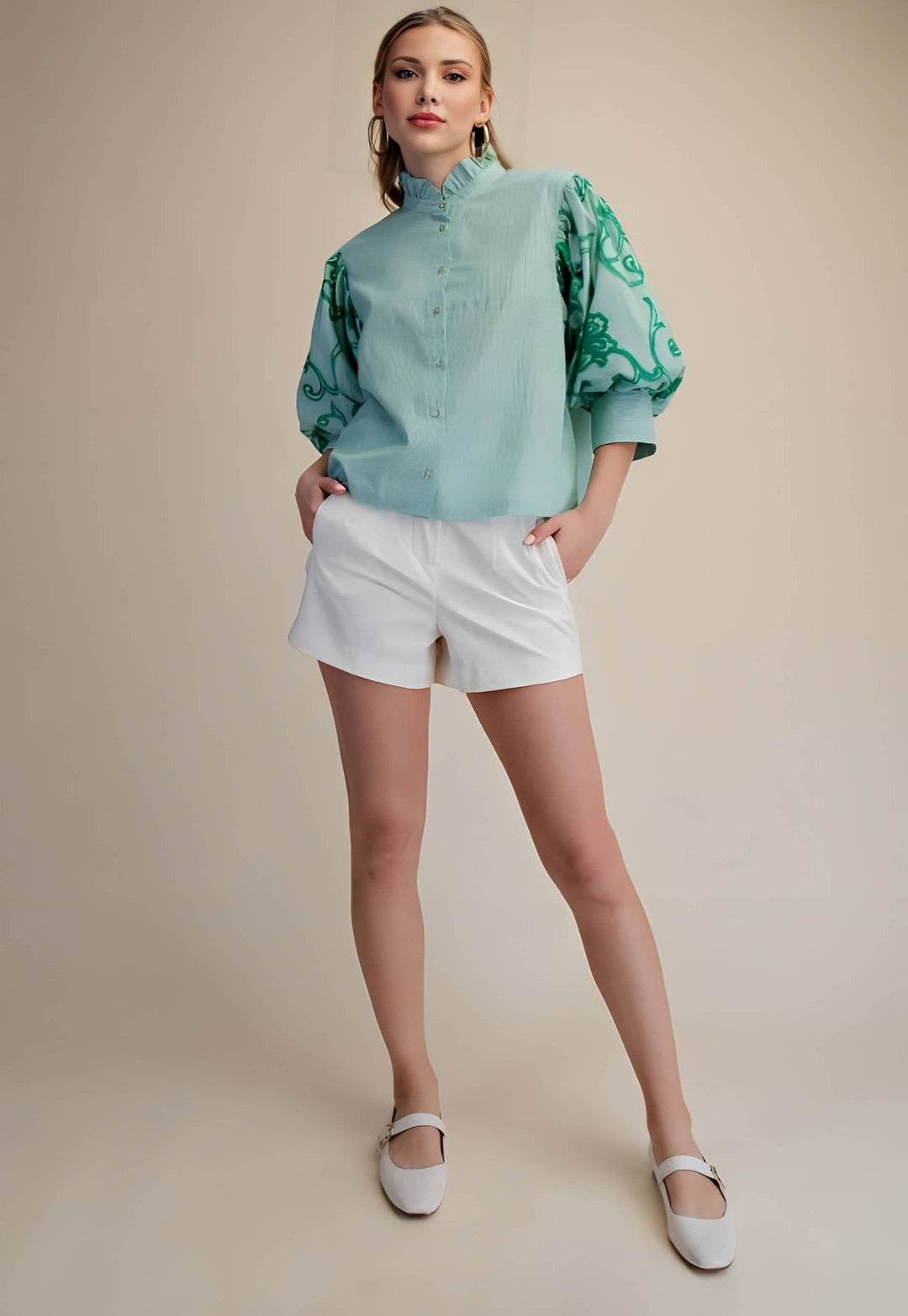 Woman wearing a light blue blouse with green patterns and white shorts on a beige background