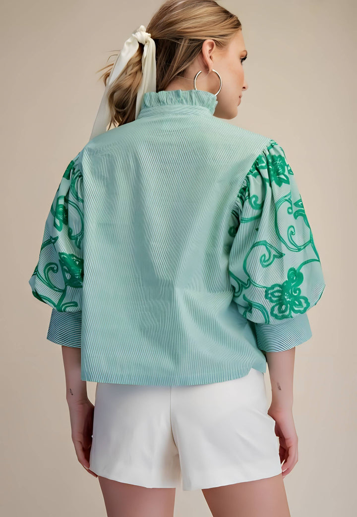 Woman wearing a light blue blouse with green floral patterns on a beige background
