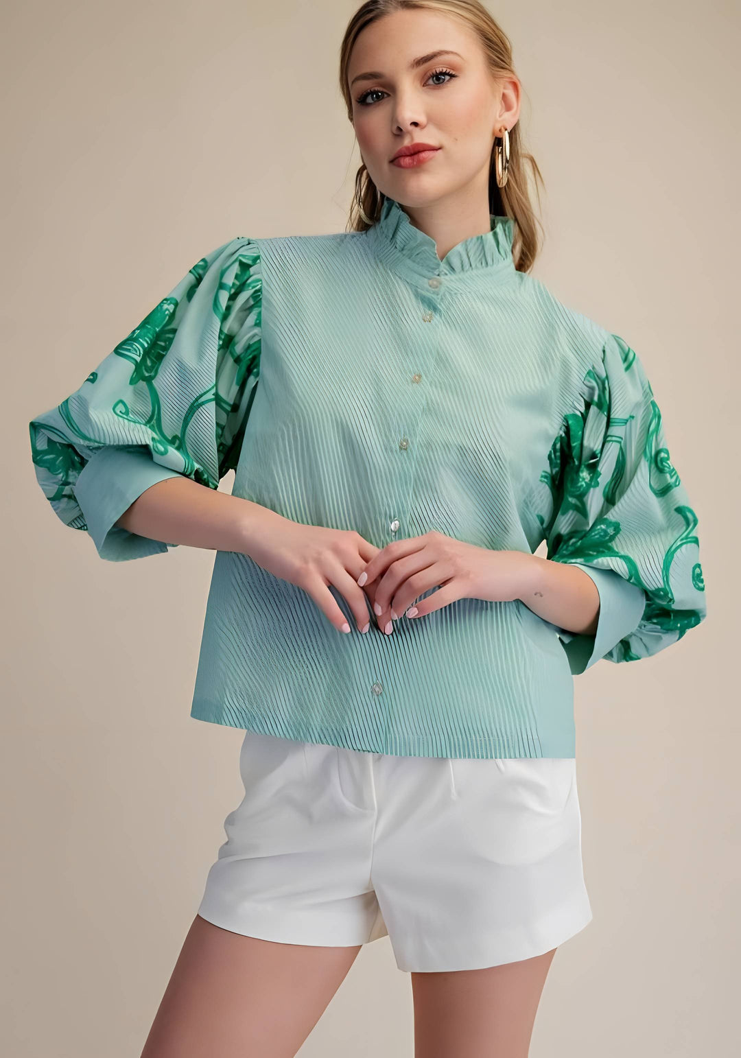 Woman wearing a light blue blouse with green floral patterns and white shorts on a beige background