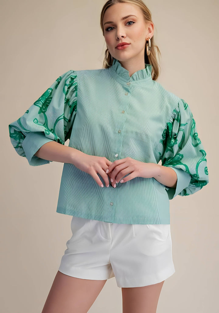 Woman wearing a light blue blouse with green floral patterns and white shorts on a beige background