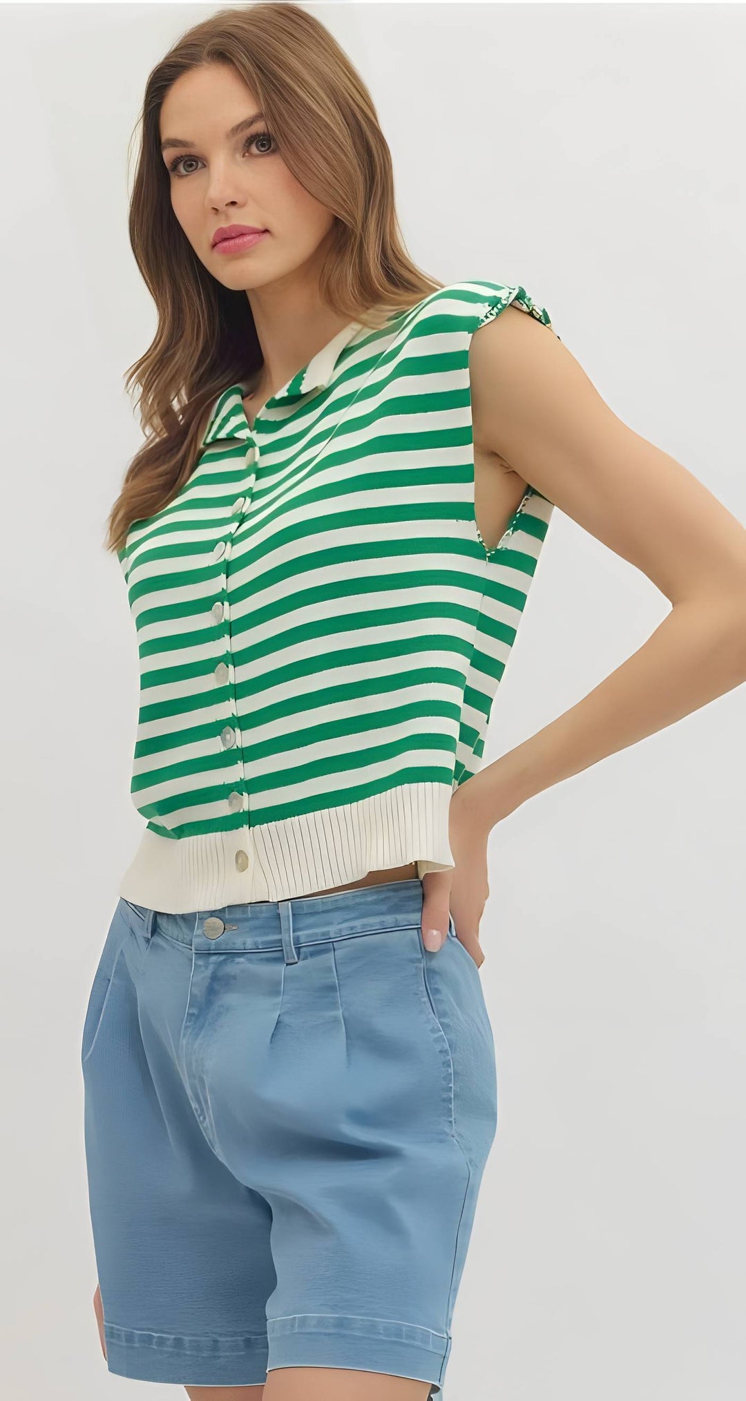 Woman wearing a green and white striped sleeveless top with blue shorts on a plain background