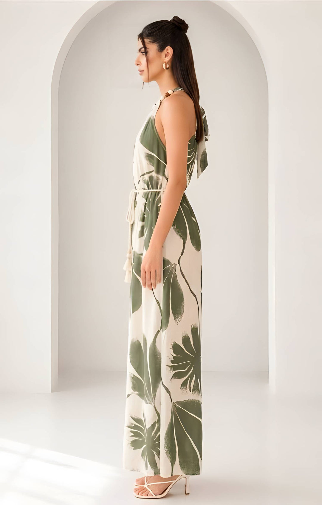 Woman wearing a long, leaf-patterned  jumpsuit standing in front of an archway.
