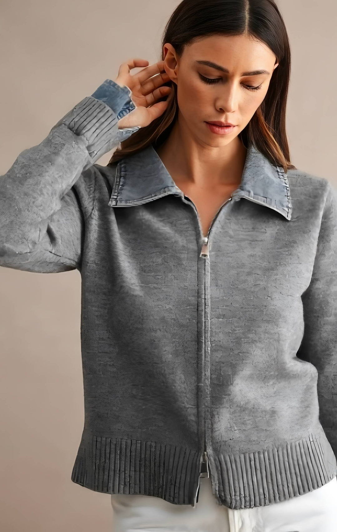 A woman wearing a gray zip-up knit cardigan with a denim collar and cuffs, paired with white pants, against a neutral beige background.