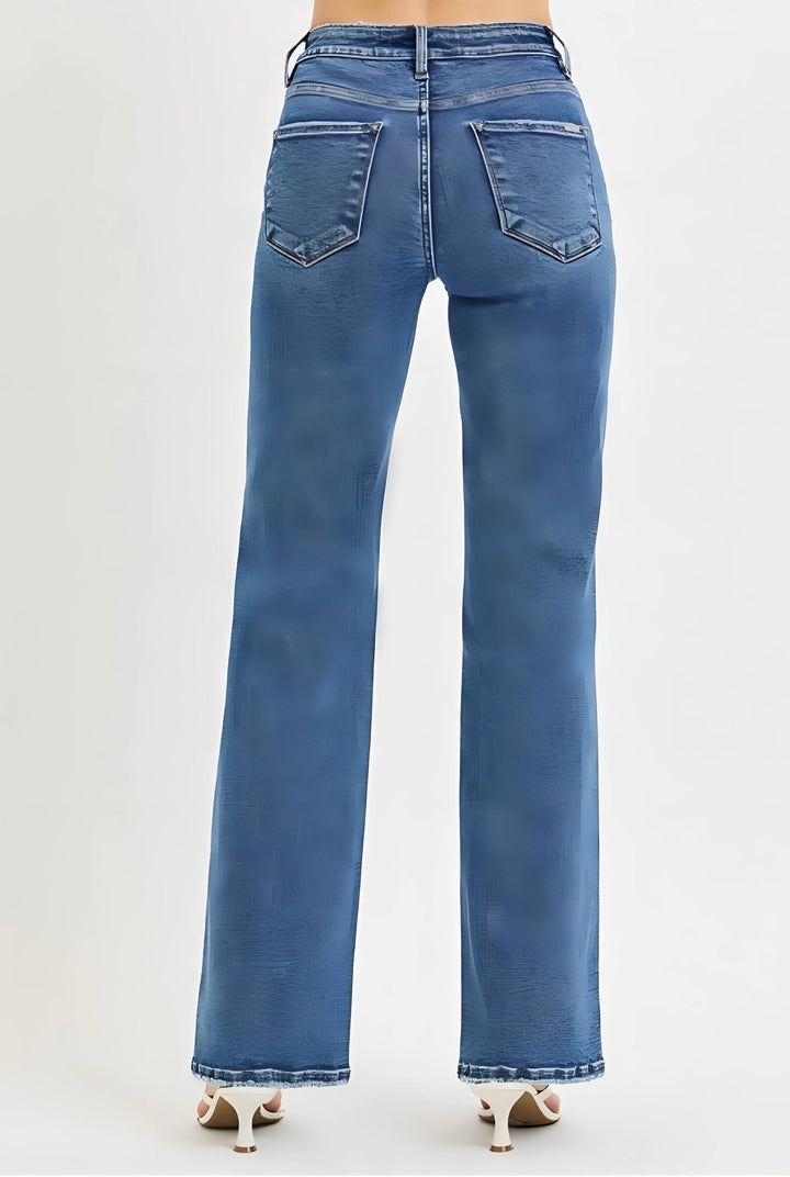 Back view of a person wearing blue high-waisted flare jeans with a faded wash and light brown heeled sandals, shown against a plain light gray studio background.