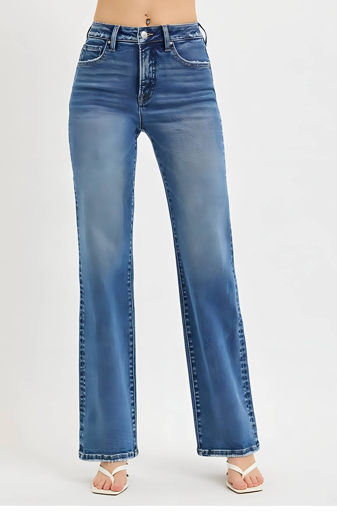 A person wearing high-waisted, wide-leg blue denim jeans with a faded wash, paired with white heeled sandals, shown against a plain light gray studio background.
