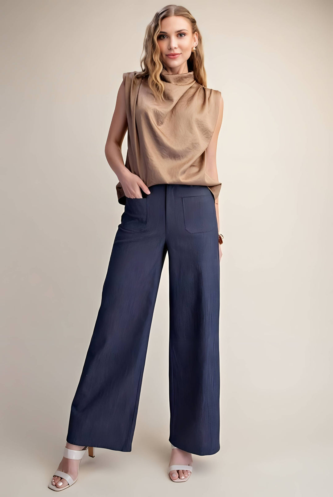 A woman modeling a sleeveless tan top and dark blue wide-leg pants against a plain beige studio background.