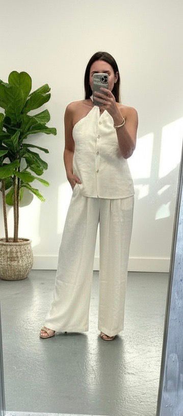 Person wearing a white outfit taking a mirror selfie in a minimalistic room.