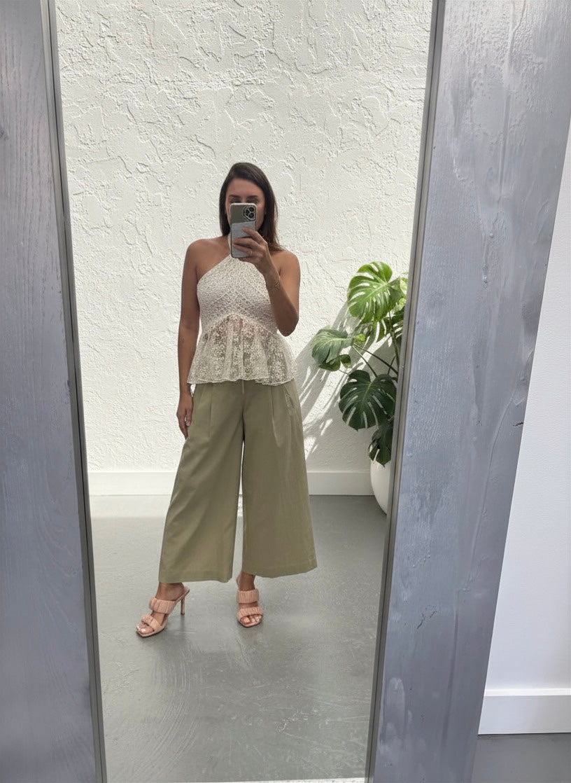 Woman taking a mirror selfie wearing a white lace top and beige pants.