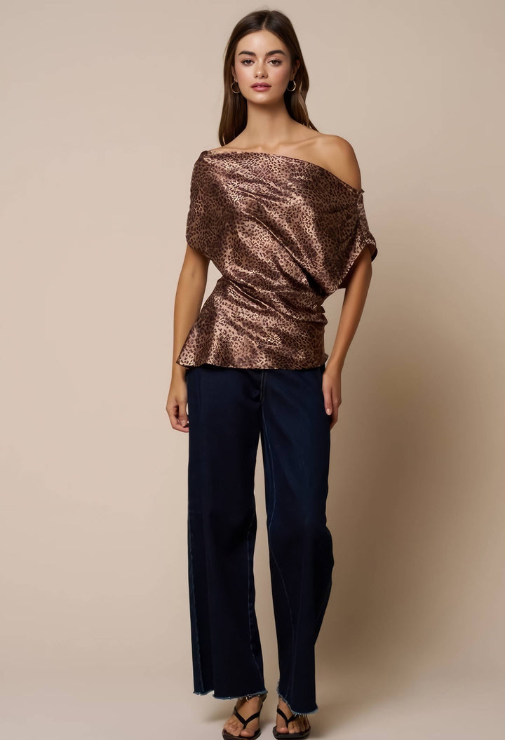 A woman modeling an off-the-shoulder metallic bronze sequined top paired with dark navy wide-leg pants and brown strappy sandals, set against a solid beige studio background.