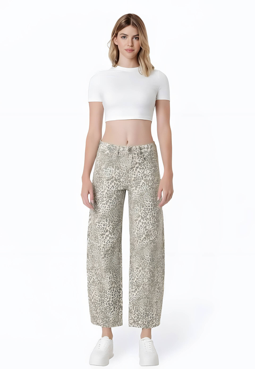 A model stands against a white studio background wearing a white short-sleeve crop top and beige-and-white animal-print wide-leg pants with white sneakers.