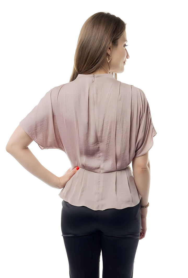 A woman shown from the back wearing a short-sleeve dusty rose peplum blouse and black pants against a white studio background.