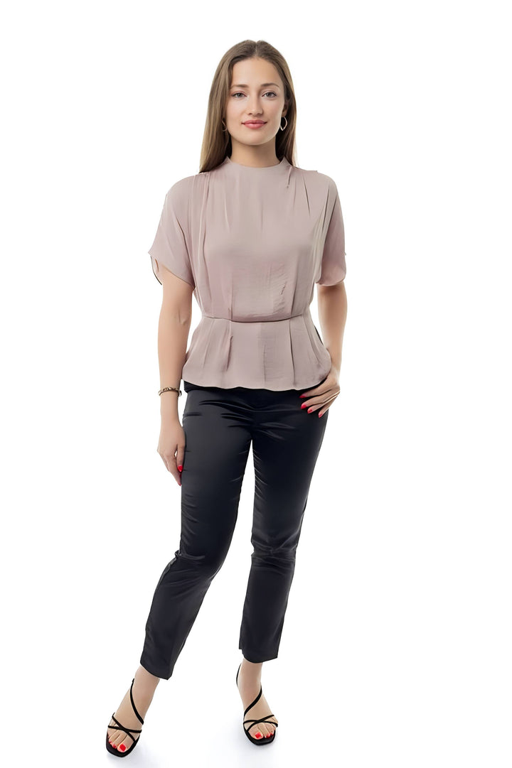 A woman modeling a short-sleeve peplum top in a dusty rose pink color, paired with black cropped pants and black strappy heels, against a solid white background.