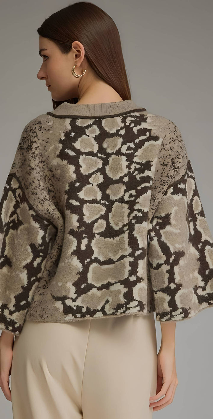 A woman shown from the back wearing a cropped knit sweater with a beige, brown, and gray animal print pattern, paired with light beige trousers, against a neutral gray studio background.